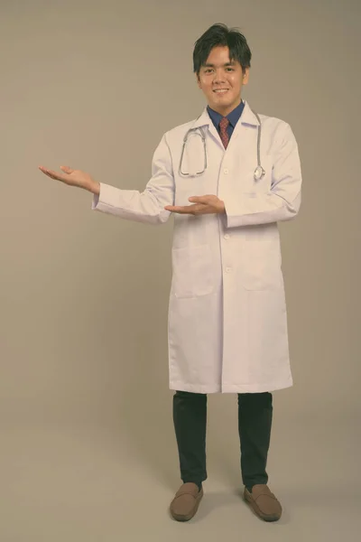 Joven guapo asiático hombre médico contra gris fondo —  Fotos de Stock