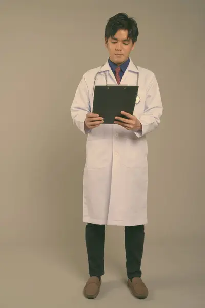 Jonge knappe Aziatische man arts tegen grijze achtergrond — Stockfoto