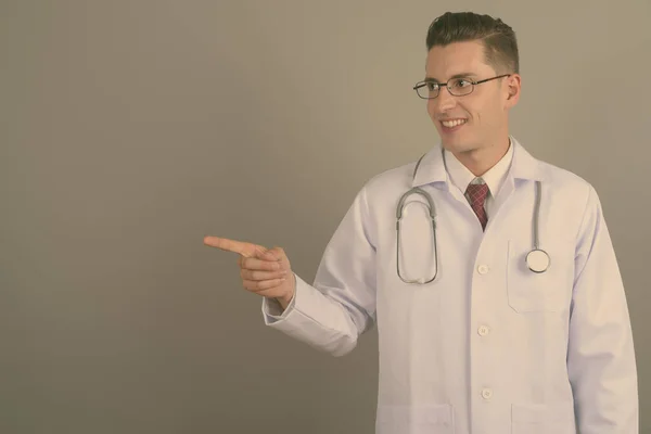 Joven hombre guapo médico contra fondo gris — Foto de Stock