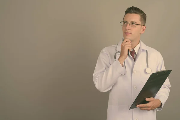 Mladý pohledný muž lékař na šedém pozadí — Stock fotografie