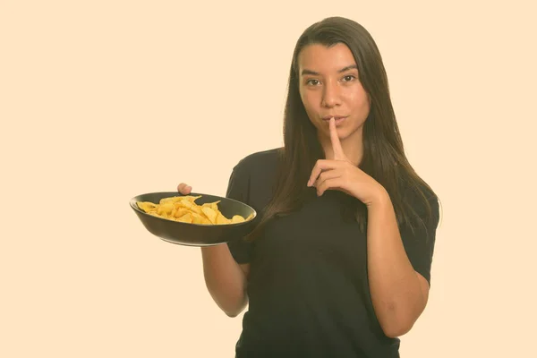 Молодая красивая белая женщина держит миску картофельных чипсов с пальцем на губах — стоковое фото