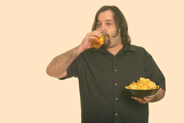 Een dikke blanke man die bier drinkt terwijl hij chips vasthoudt. — Stockfoto