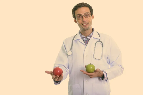 Στούντιο πλάνο του νεαρού χαρούμενος γιατρός χαμογελώντας, ενώ κρατώντας πράσινο μήλο και κόκκινο μήλο — Φωτογραφία Αρχείου