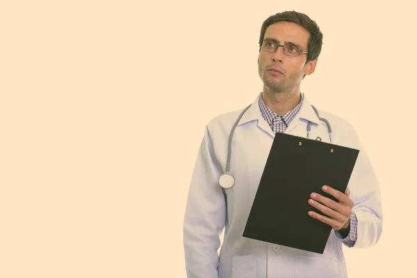 Studioaufnahme eines jungen gutaussehenden Mannes Doktor denken, während er Klemmbrett mit Brille hält — Stockfoto