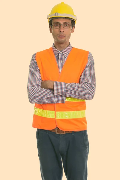 Studio colpo di giovane bel lavoratore edile uomo in piedi mentre indossa occhiali con le braccia incrociate — Foto Stock