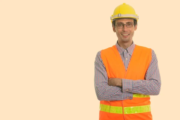 Estudio de disparo de hombre feliz joven trabajador de la construcción sonriendo mientras llevaba gafas con los brazos cruzados —  Fotos de Stock