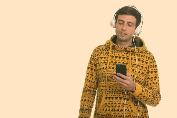 Studio shot van jonge knappe man luisteren naar muziek tijdens het gebruik van mobiele telefoon — Stockfoto