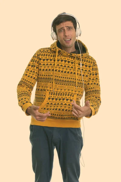 Studio shot of young handsome man standing while listening to music and gesturing hands — Stock Photo, Image