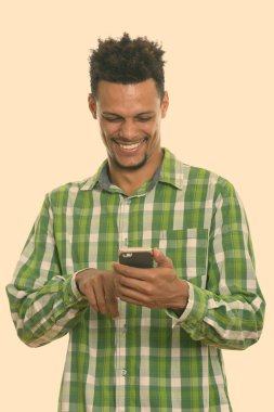 Cep telefonu kullanırken gülümseyen Afrikalı genç adamın stüdyo fotoğrafı.