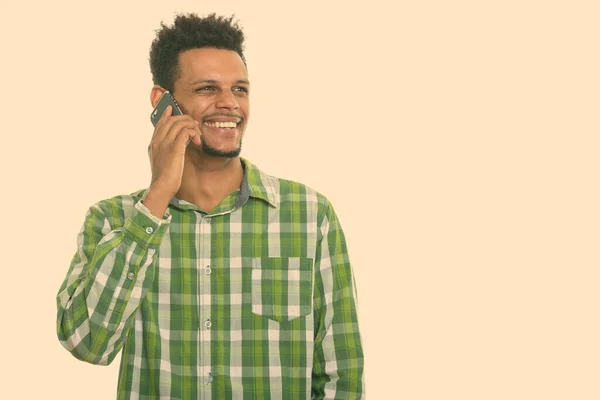 Studio skott av ung glad afrikansk man ler när du talar på mobiltelefon och tänker — Stockfoto