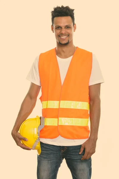 Młody szczęśliwy Afrykanin budowlany pracownik uśmiecha się trzymając kask bezpieczeństwa — Zdjęcie stockowe