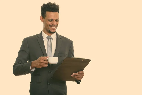 Joven empresario africano feliz sonriendo mientras lee en el portapapeles y sosteniendo la taza de café — Foto de Stock