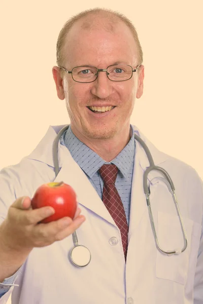 Studio strzał szczęśliwy człowiek lekarz uśmiecha się dając czerwone jabłko — Zdjęcie stockowe