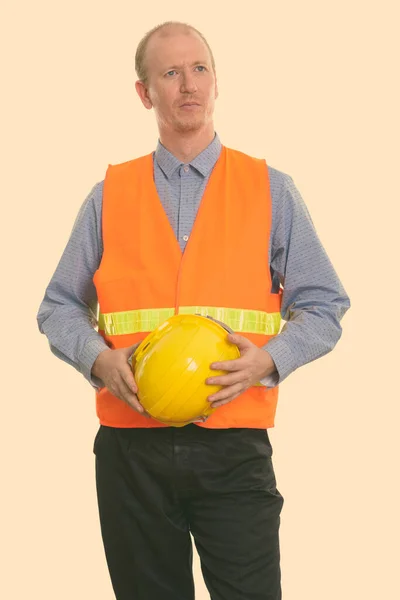 Hombre reflexivo trabajador de la construcción sosteniendo casco de seguridad con ambas manos —  Fotos de Stock