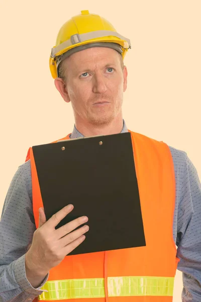 Estudio de hombre trabajador de la construcción sosteniendo portapapeles mientras pensaba —  Fotos de Stock