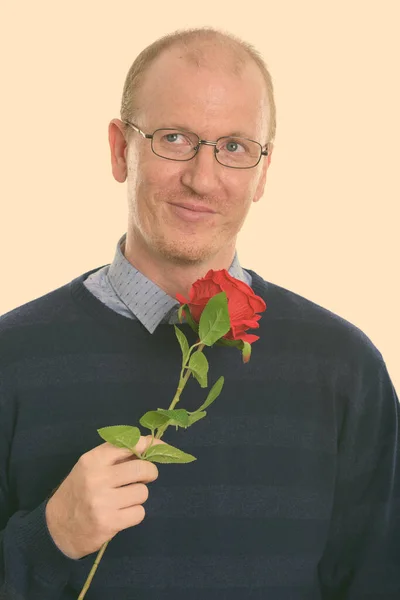 Estudio de tiro de hombre feliz sonriendo mientras sostiene rosa roja y pensando listo para el día de San Valentín — Foto de Stock