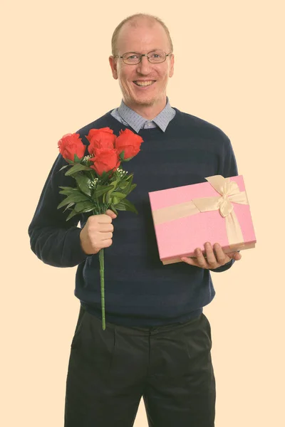 Estudio de tiro de hombre feliz sonriendo mientras sostiene rosas rojas y caja de regalo listo para el día de San Valentín — Foto de Stock