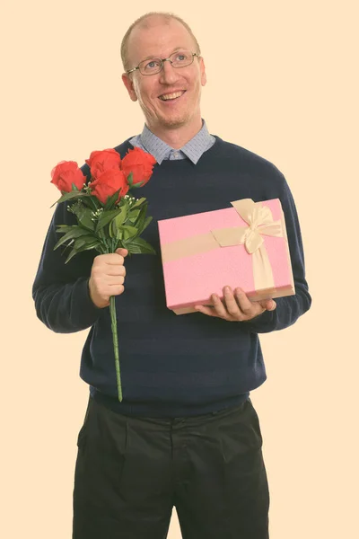 Pensativo hombre feliz sonriendo mientras sostiene rosas rojas y caja de regalo listo para el día de San Valentín — Foto de Stock