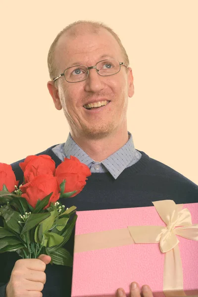 Духовний щасливий чоловік посміхається, тримаючи червоні троянди і скриньку з подарунками, готову для Валентинів день. — стокове фото