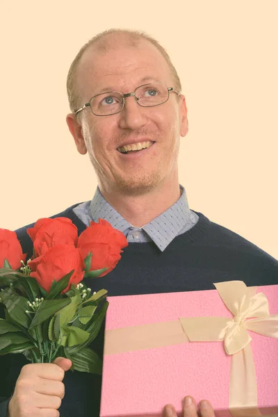 Pensativo hombre feliz sonriendo mientras sostiene rosas rojas y caja de regalo listo para el día de San Valentín — Foto de Stock