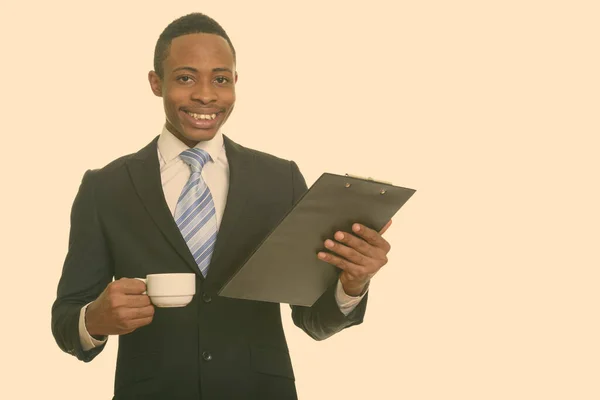 Młody szczęśliwy afrykański biznesmen uśmiecha się trzymając schowek i filiżankę kawy — Zdjęcie stockowe