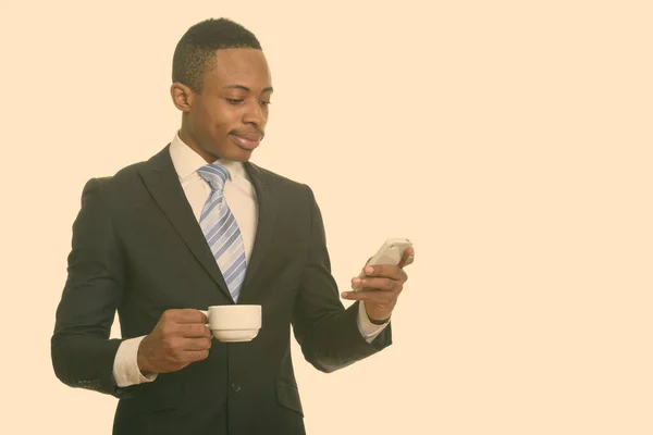 Młody przystojny afrykański biznesmen za pomocą telefonu komórkowego, trzymając filiżankę kawy — Zdjęcie stockowe
