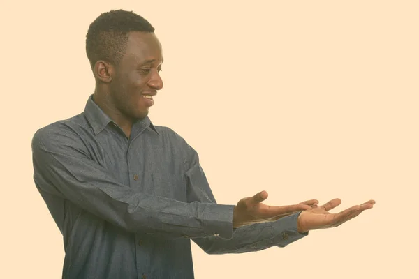 Vista del perfil del joven hombre africano feliz sonriendo y mostrando algo — Foto de Stock