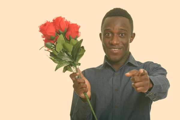 Ung glad afrikansk man ler och pekar finger medan du håller röda rosor redo för alla hjärtans dag — Stockfoto