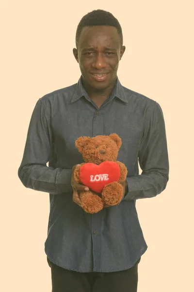 Szomorú afrikai férfi kezében teddy maci szívvel és szeretettel jel — Stock Fotó