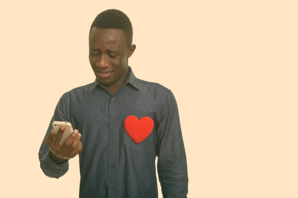 Üzgün Afrikalı adam göğsünde kırmızı kalp olan cep telefonu kullanıyor. — Stok fotoğraf