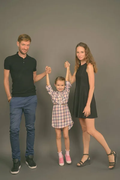 Junge glückliche Familie, die vor grauem Hintergrund zusammenhält — Stockfoto