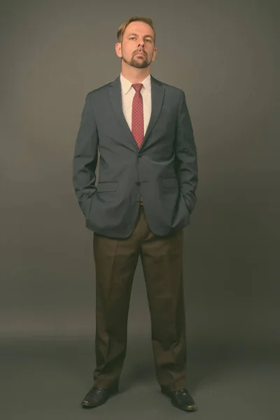 Блондин бородатий бізнесмен з гоатом на сірому фоні — стокове фото