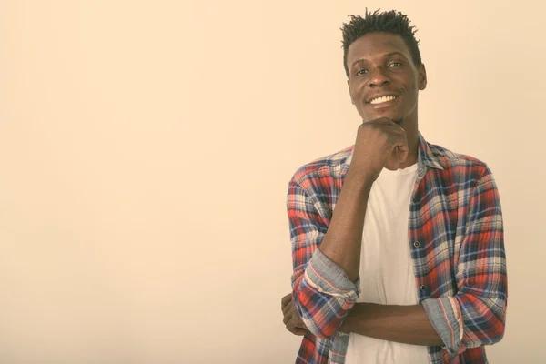 Studio shot van jonge gelukkig zwart Afrikaanse man glimlachen terwijl denken tegen witte achtergrond — Stockfoto