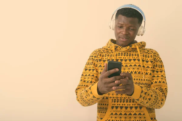 Estúdio tiro de jovem negro africano usando telefone celular enquanto ouve música contra fundo branco — Fotografia de Stock