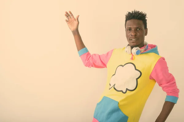 Estudio de un joven negro africano posando mientras llevaba auriculares alrededor del cuello con el brazo levantado sobre fondo blanco — Foto de Stock