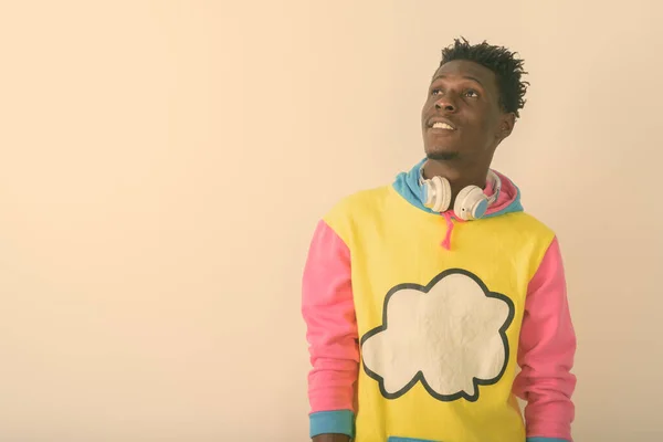 Estúdio tiro de jovem negro feliz Africano homem sorrindo e pensando ao usar fones de ouvido em torno do pescoço contra fundo branco — Fotografia de Stock