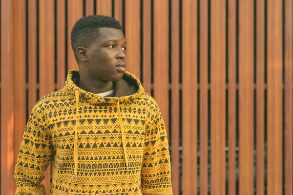 Close up de jovem negro Africano homem pensando enquanto olha para a distância contra portão de madeira — Fotografia de Stock