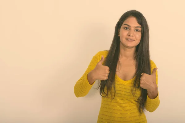 Estudio disparo de la joven mujer india feliz sonriendo mientras que da pulgares hacia arriba contra fondo blanco — Foto de Stock