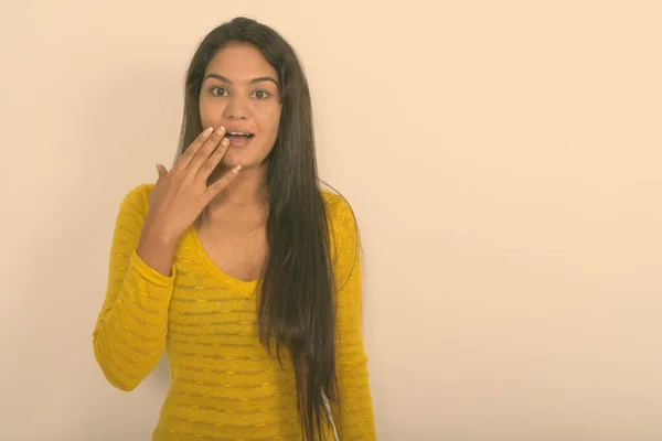 Studio shot of young happy Indian woman smiling while looking surprised and covering mouth against white background — Stock Photo, Image