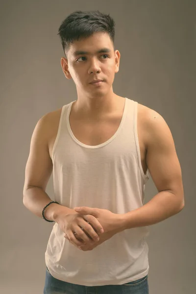 Jonge knappe Aziatische man draagt tank top tegen grijze achtergrond — Stockfoto