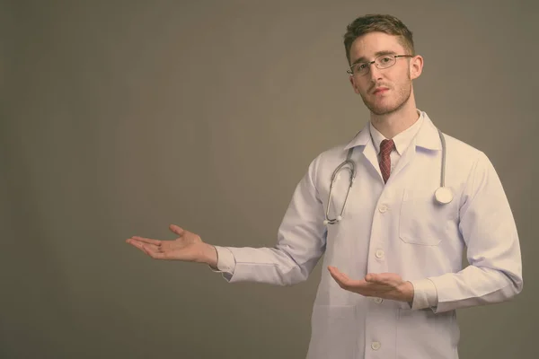 Joven hombre guapo médico con anteojos sobre fondo gris — Foto de Stock