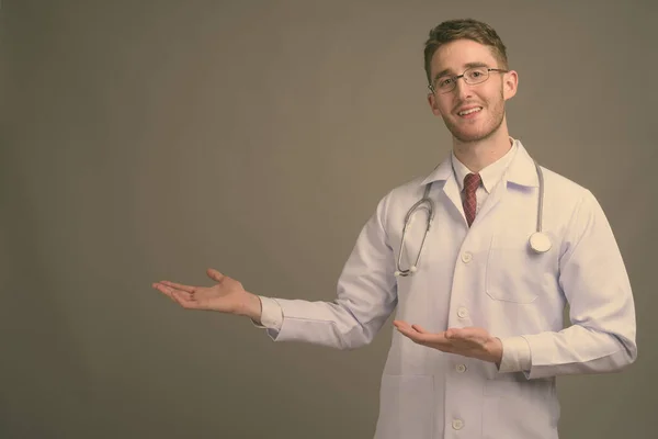 年轻英俊的医生，戴着灰色背景的眼镜 — 图库照片