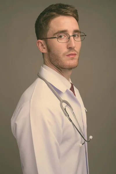 Joven hombre guapo médico con anteojos sobre fondo gris —  Fotos de Stock