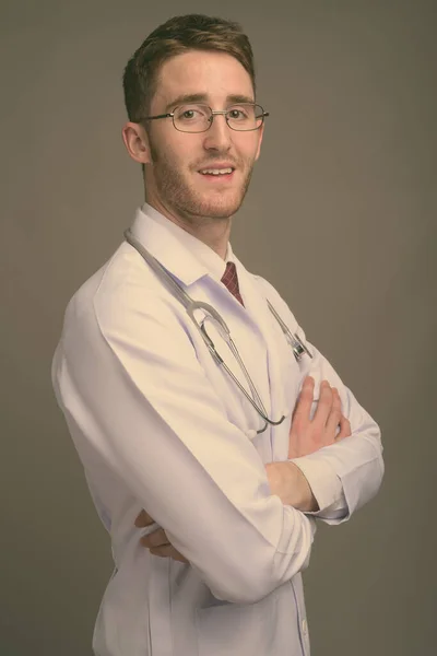Młody przystojny mężczyzna lekarz noszenie okulary na szarym tle — Zdjęcie stockowe