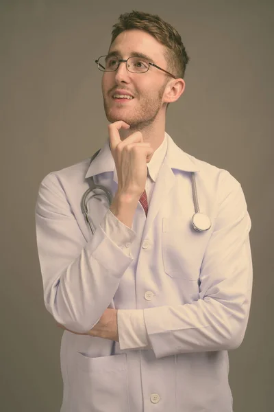 Fiatal jóképű férfi orvos visel szemüveg ellen szürke háttér — Stock Fotó