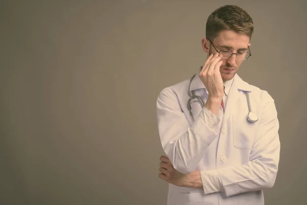 Jovem bonito homem médico vestindo óculos contra fundo cinza — Fotografia de Stock