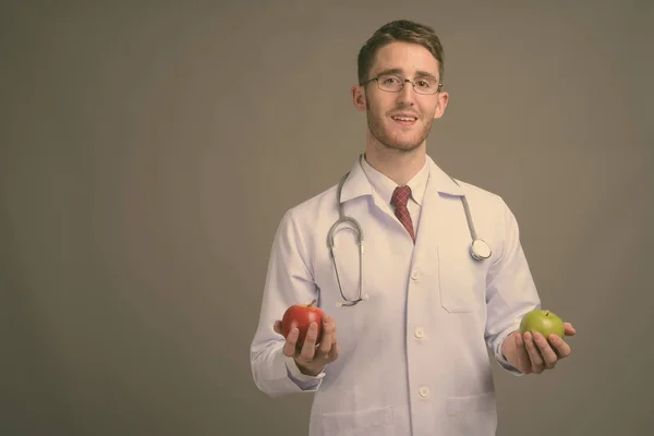 Joven hombre guapo médico con anteojos sobre fondo gris —  Fotos de Stock