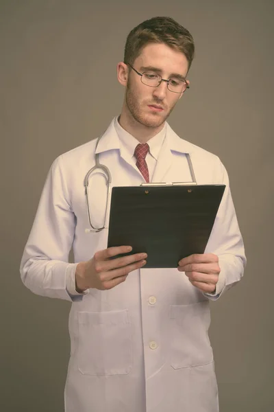 Young handsome man doctor wearing eyeglasses against gray background — Stock Photo, Image