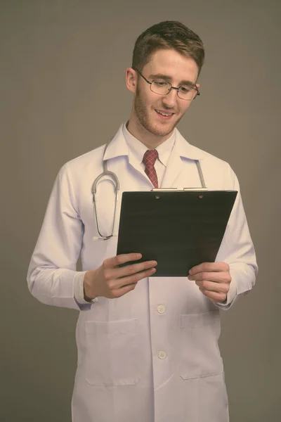 Jovem bonito homem médico vestindo óculos contra fundo cinza — Fotografia de Stock