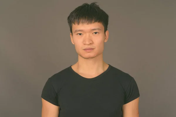 Studio shot of young Chinese man against gray background — Stock Photo, Image